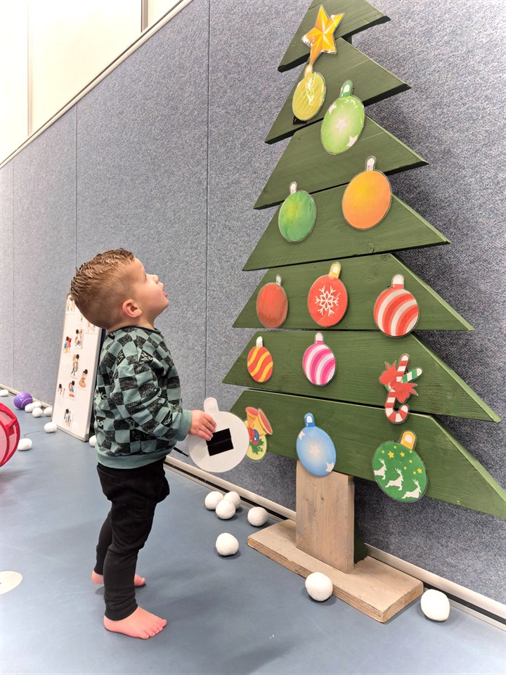 Kind dat tijdens een kerstkampje bij een versierde kerstboom speelt