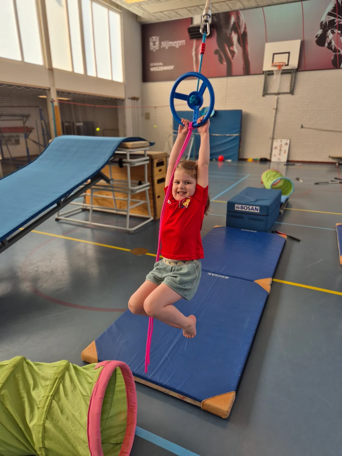 Kind dat met plezier aan een klimwiel hangt tijdens de gymles